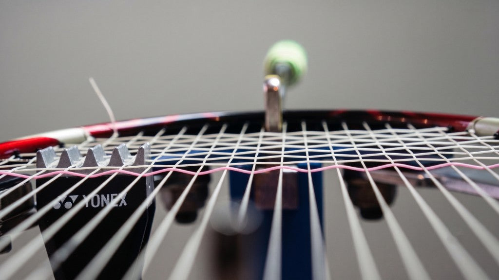 Close-up badminton racket strings, shuttlecock, and stringing tools for a string tension guide.