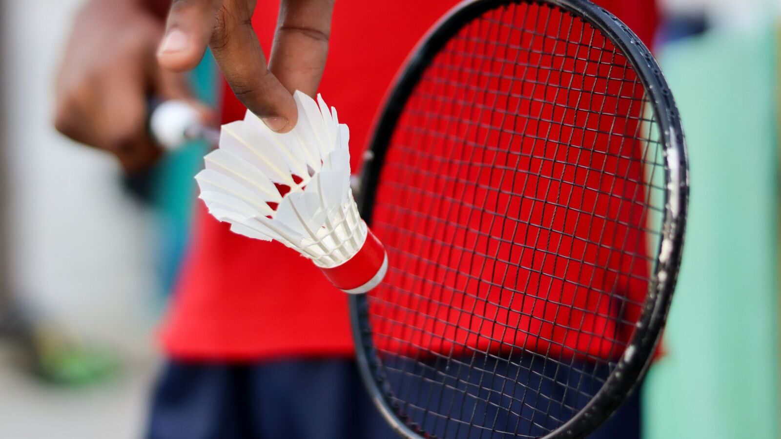 Gros plan d’une main tenant un volant de badminton à côté du cordage d’une raquette, prête pour une séquence d’alimentation