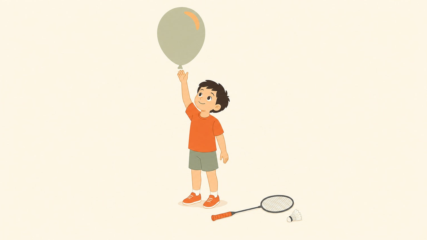 A young child taps a floating balloon with an open hand while a short junior badminton racket and a single shuttlecock rest on the ground nearby.