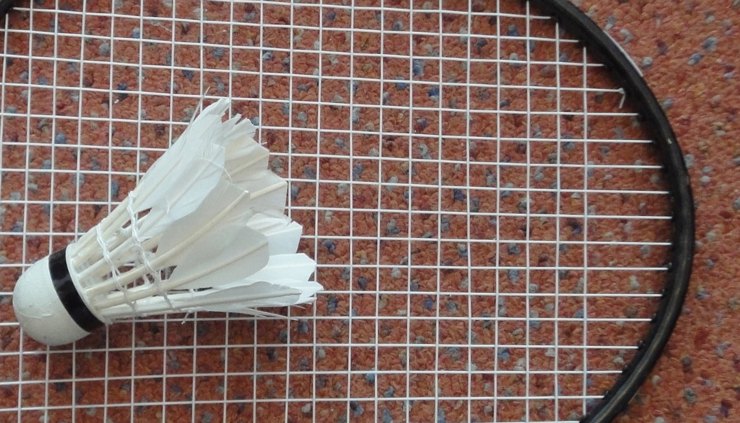 Gros plan d’un volant de badminton posé sur le cordage d’une raquette, le point de contact entre la raquette et le volant que les exercices de contrôle pour débutants entraînent.
