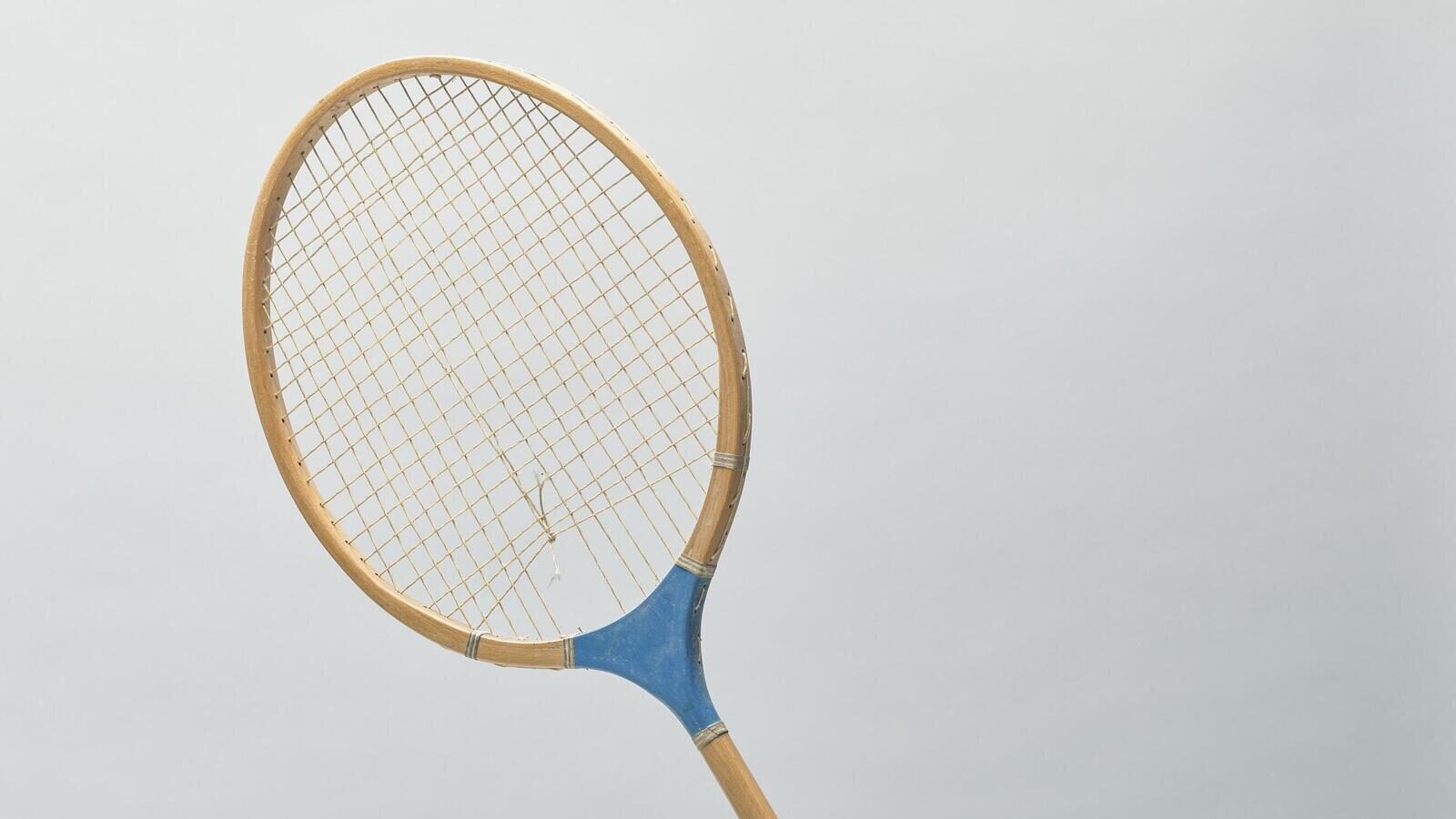 Gros plan d’une raquette de badminton en bois dont une corde est cassée dans le plan de cordage croisé, photographiée sur un fond uni