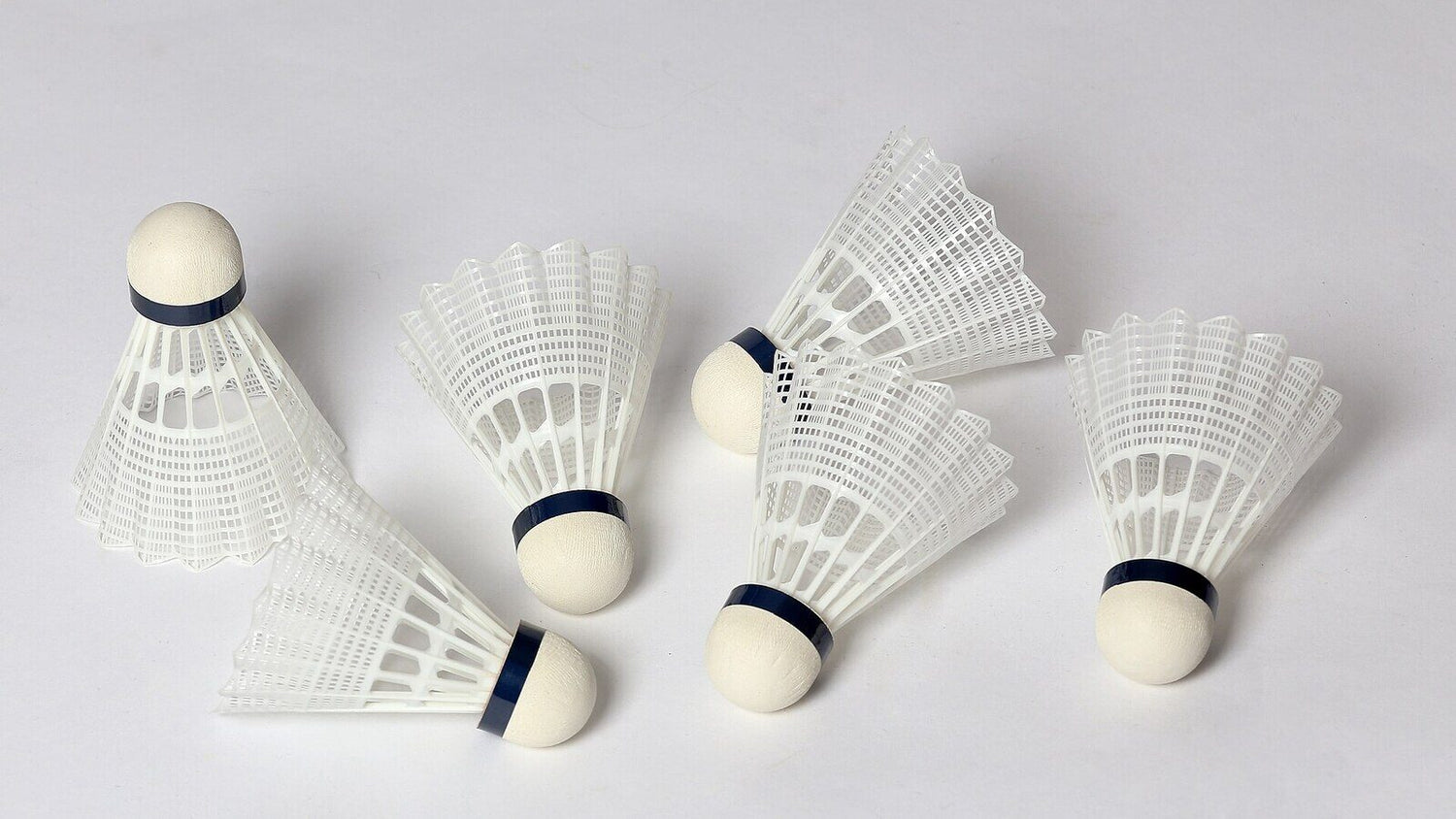 Six volants de badminton éparpillés sur une surface unie, leurs jupes de plumes et leurs bases en liège visibles, comme l’équipement qui reste inutilisé lorsqu’une blessure empêche une personne de jouer.