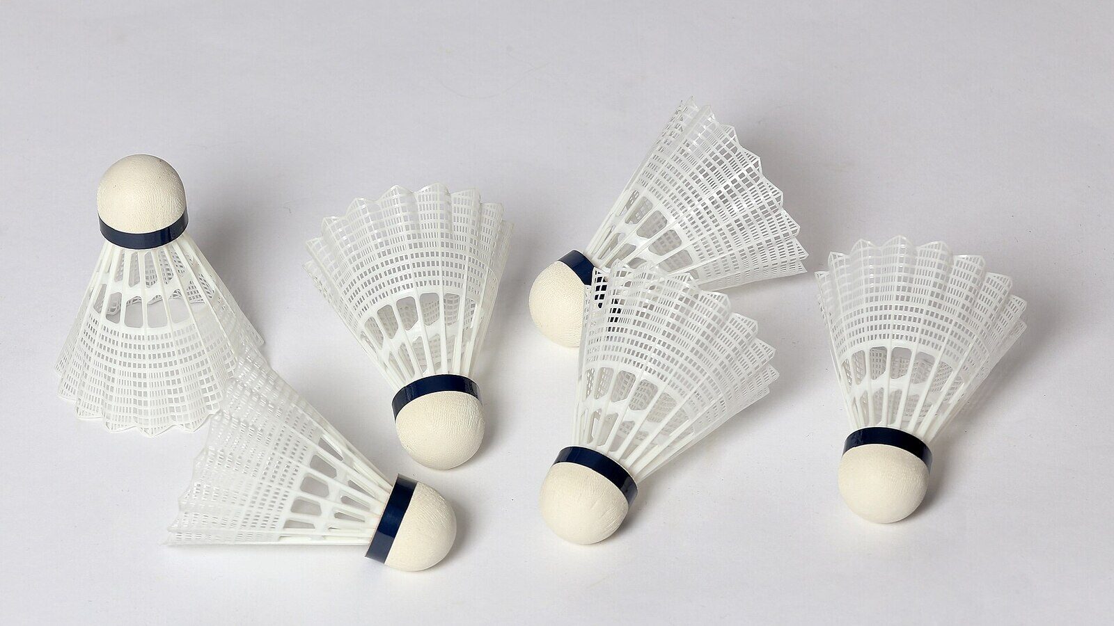 Six volants de badminton éparpillés sur une surface unie, leurs jupes de plumes et leurs bases en liège visibles, comme l’équipement qui reste inutilisé lorsqu’une blessure empêche une personne de jouer.