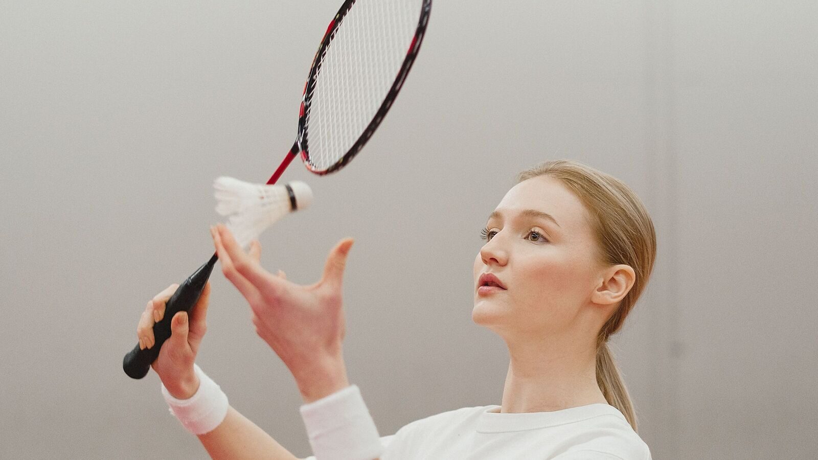 Une joueuse de badminton lance le volant juste sous sa raquette levée, le suivant des yeux alors qu’elle se prépare à servir.