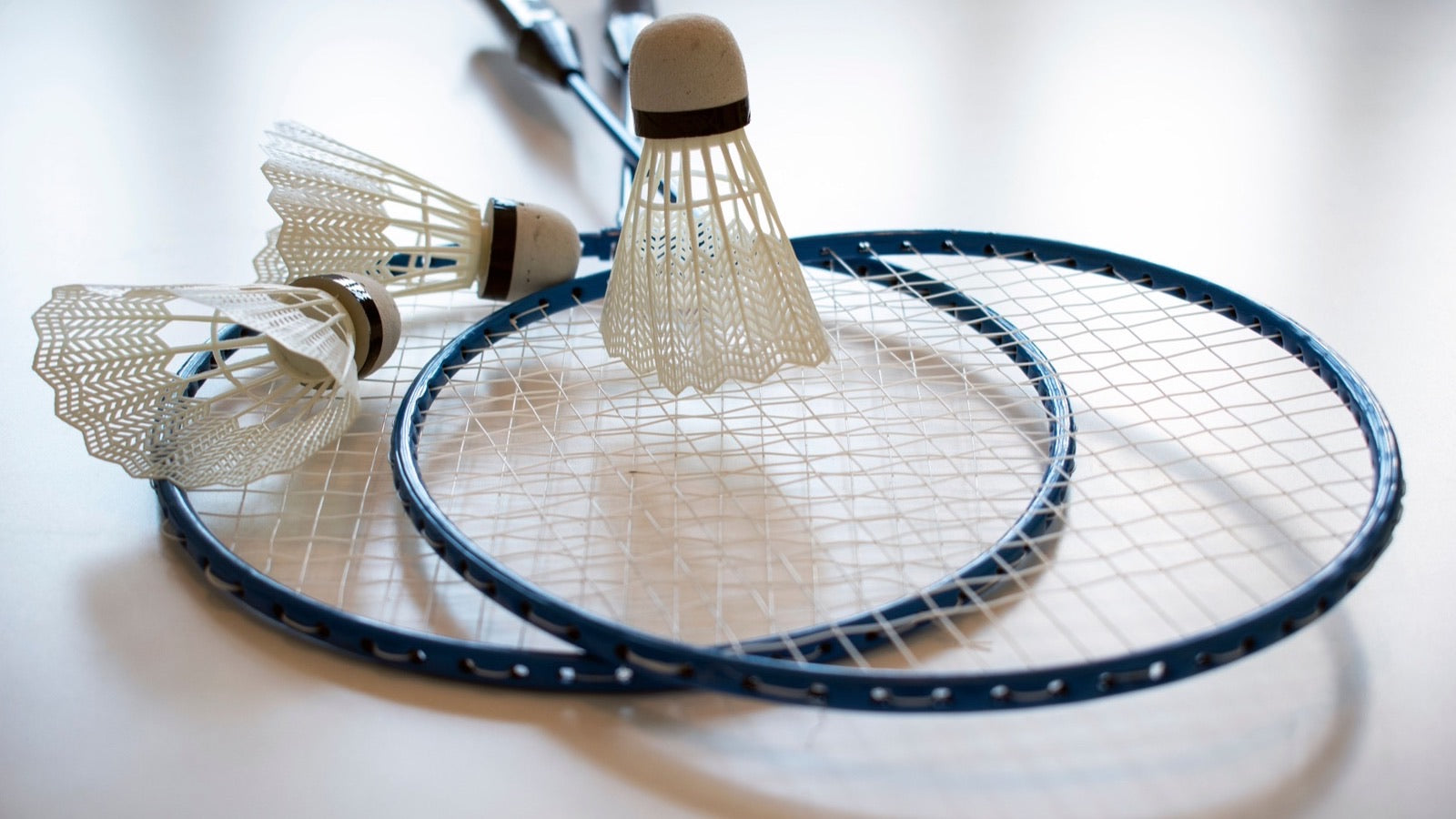 Gros plan de deux raquettes de badminton métalliques d’entrée de gamme et de volants en plastique posés sur un plancher intérieur
