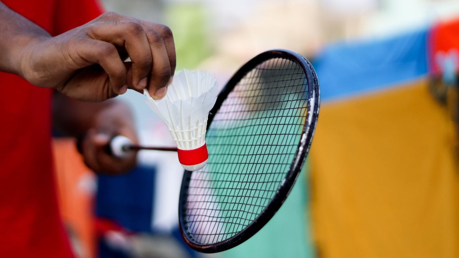 La main d’une personne tient un volant en plumes à côté du plan de cordage d’une raquette de badminton sans marque, en vérifiant les cordes avant le jeu.